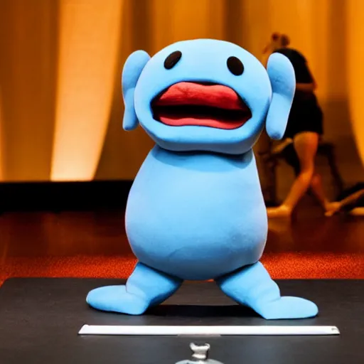 Image similar to a little blue creature in the shape of a sausage lies on a huge microphone on the stage