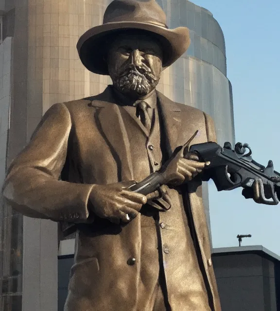 Image similar to a 4 k photorealistic photo medium shot of a bronze statue of a man wearing a fedora holding one revolver in each hand.