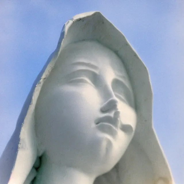 Image similar to closeup of white mother mary statue crying, pictured slightly from below, clear sky with blue clouds in background, vintage polaroid