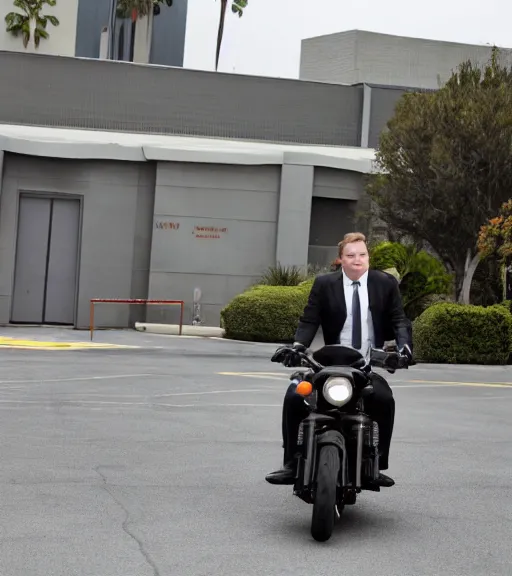 Image similar to Andy Richter is dressed in a black suit and a red necktie and riding a motorcycle into a studio lot. The studio lot is filled with Soundstages and movie trailers. It is a bright afternoon and overcast.