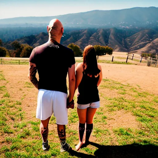 Image similar to portrait of a bald white male tattoos and his white female brown hair wife with tattoos. male is wearing a white t - shirt, tan shorts, white long socks. female is has long brown hair and a lot of tattoos. photo taken from behind them overlooking the field with a goat pen. rolling hills in the background of california and a partly cloudy sky