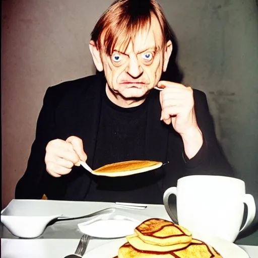 Image similar to mark e smith sitting at a table eating a big stack of pancakes, fork and knife in hand, drooling and licking his lips, photograph