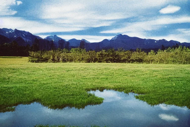 Image similar to film color photography, small mirror reflected clouds, long view of green lawn, no focus, mountains in distance, 35mm