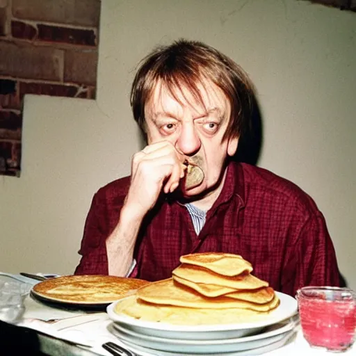 Image similar to mark e smith sitting at a table eating a big stack of pancakes, fork and knife in hand, drooling and licking his lips, photograph