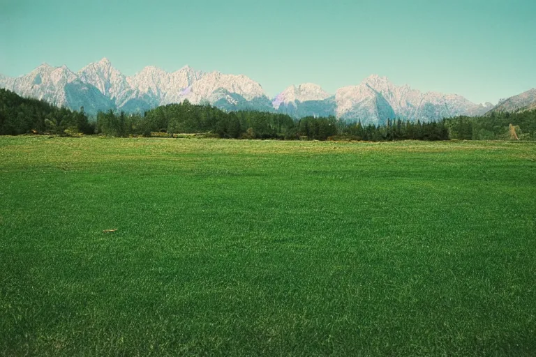 Image similar to film color photography, small mirror in distance, long view of green lawn, no focus, mountains in distance, 35mm