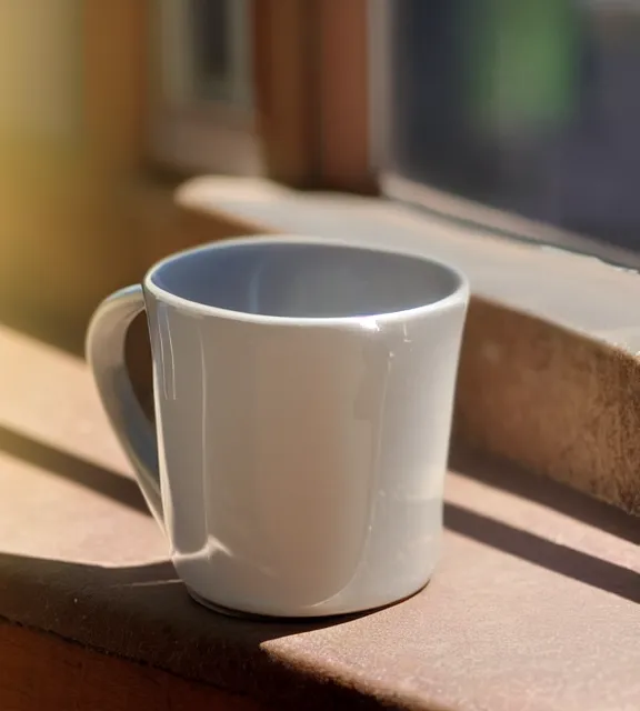 Image similar to a 4 k photorealistic photo close up of a mug on a sunny windowsill.