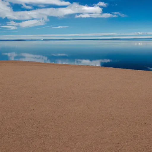 Image similar to a still plain of endless water across the horizon, with a slightly cloudy blue sky above it and reflected within it