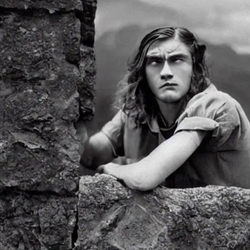 Image similar to Still of a movie set in the 1930s where a terrified young man with long hair is crouched up against a stone wall. He is looking utterly panicked and distressed