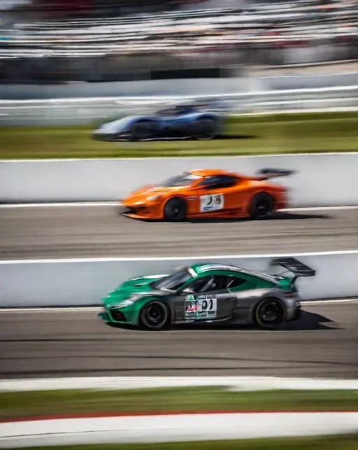 Prompt: Low angled panning shot of sleek race cars speeding around a track. Motion blur creates a sense of high velocity in the exhilarating style of automotive photographer Tim Scott, shot with a Sony A1 and 24-70mm lens.  